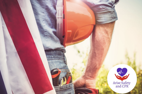 Man facing towards a field, holding a hard hat with tools in his back pocket and an American Flag draped over his shoulder. Happy Labor Day